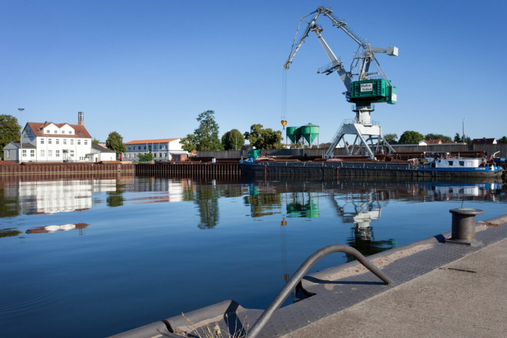 Abbildung des Hafens in Velten. Wasserfläche mit einem Kran im Hintergrund. 