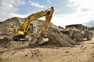 Bagger vor einen Sandberg schaufelt Sand.