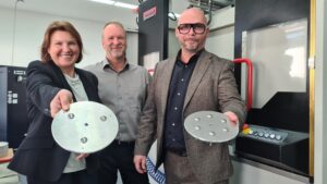 Die Antonics-Geschäftsführer Knut Feige (Mitte) und René Roeder zeigen Bürgermeisterin Ines Hübner den bereits bearbeiteten Metallrohling, der die Basis für die Antennentechnik bildet.